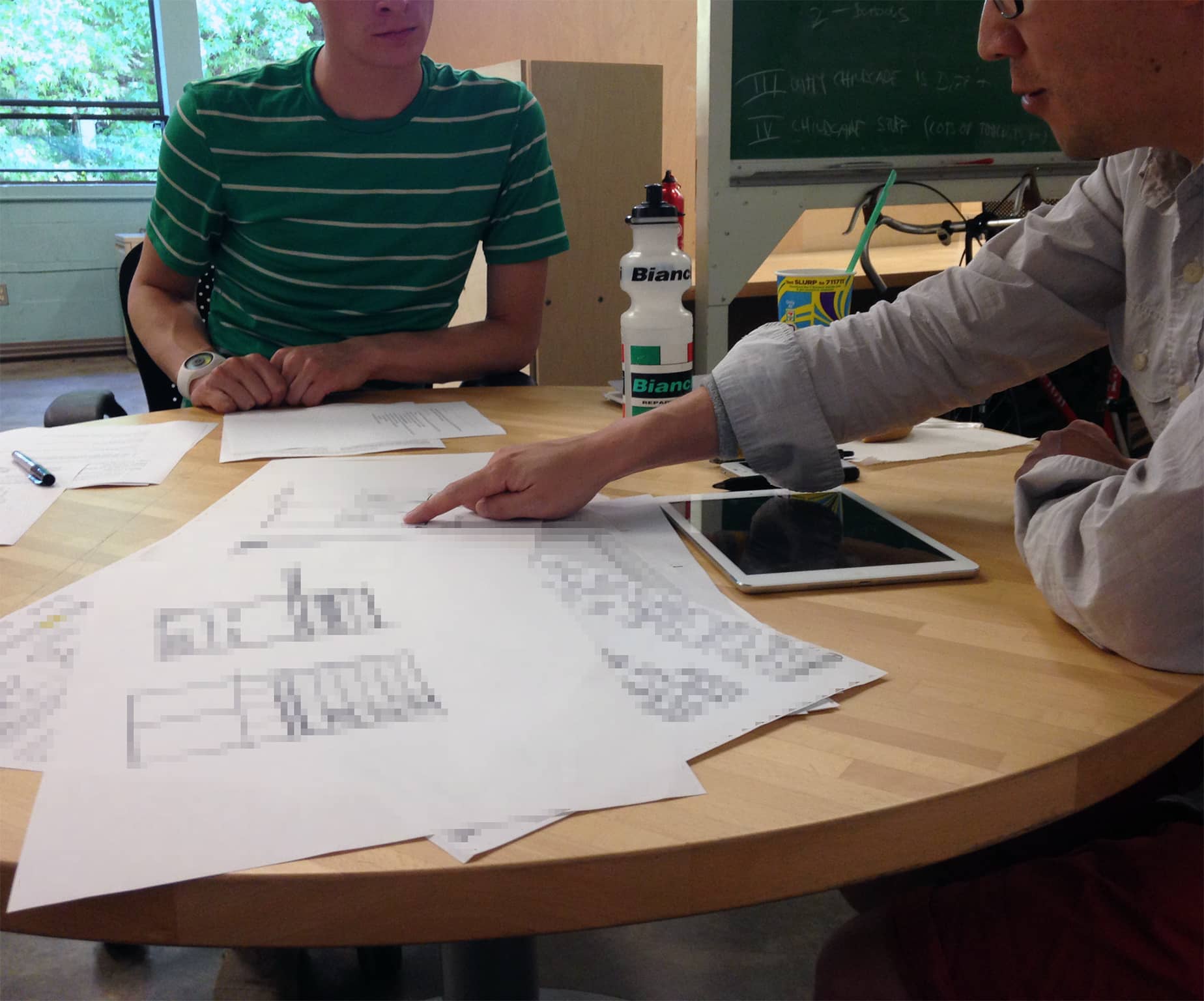 Designer at a table pointing out a detail in a sketch to another designer sitting at the table