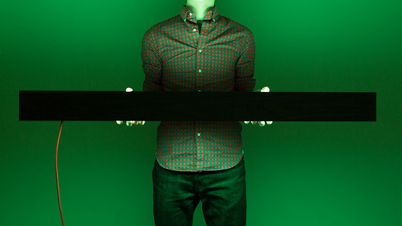 A man holding the BarLight at waist height as the light illuminates the room in a soft green color