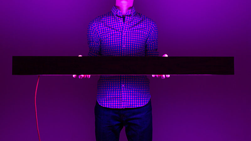 A man holding the BarLight at waist height as the light illuminates the room in a soft purple color